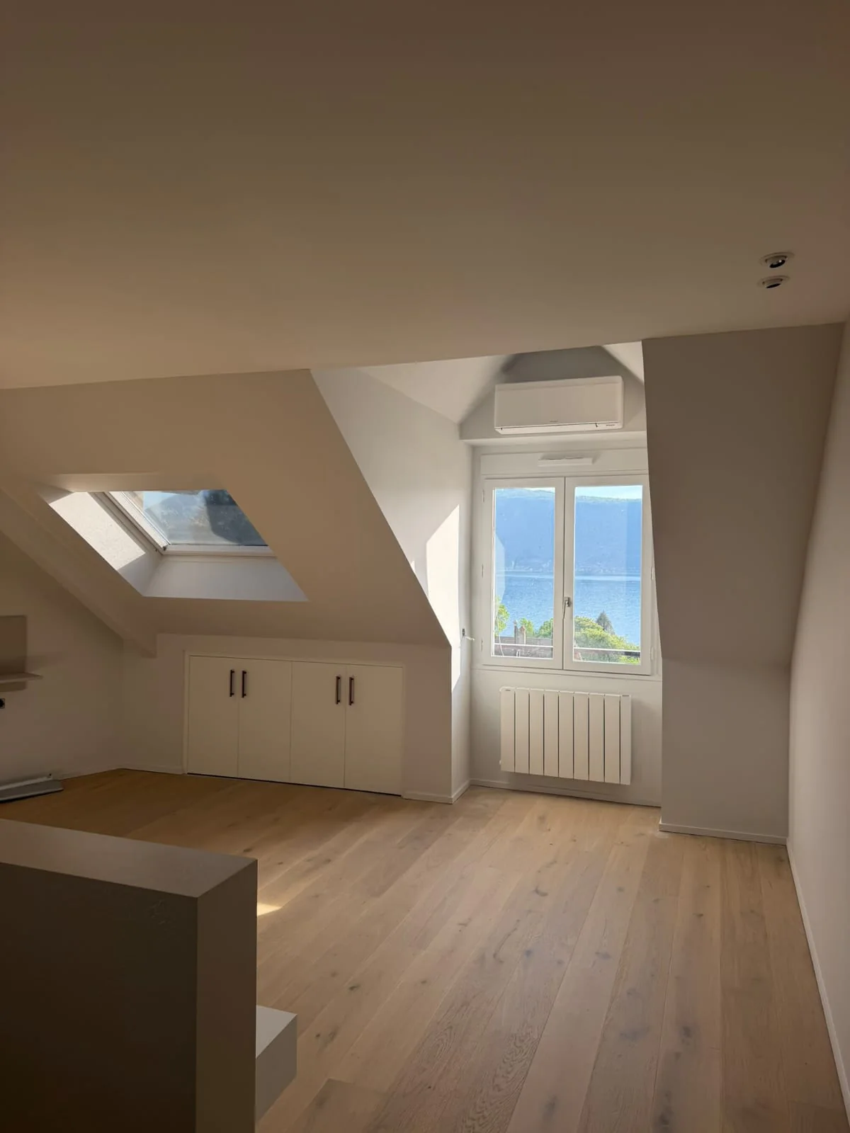Chambre sous combles avec parquet bois clair, fenêtre de toit et rangements bas