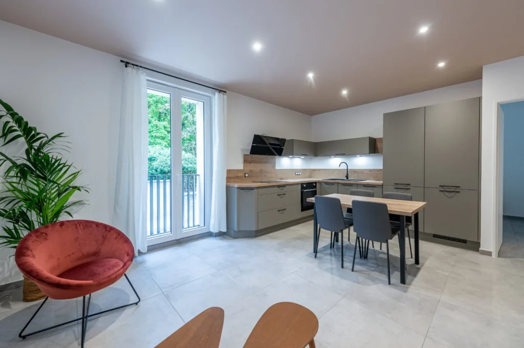 Cuisine ouverte et coin repas près d’une porte-fenêtre, sol en grands carreaux