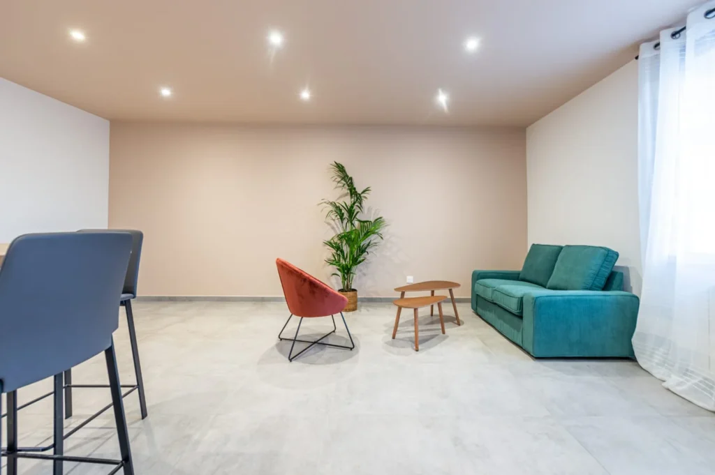 Séjour rénové au mur rose poudré, sol en grands carreaux clairs et plafond à spots