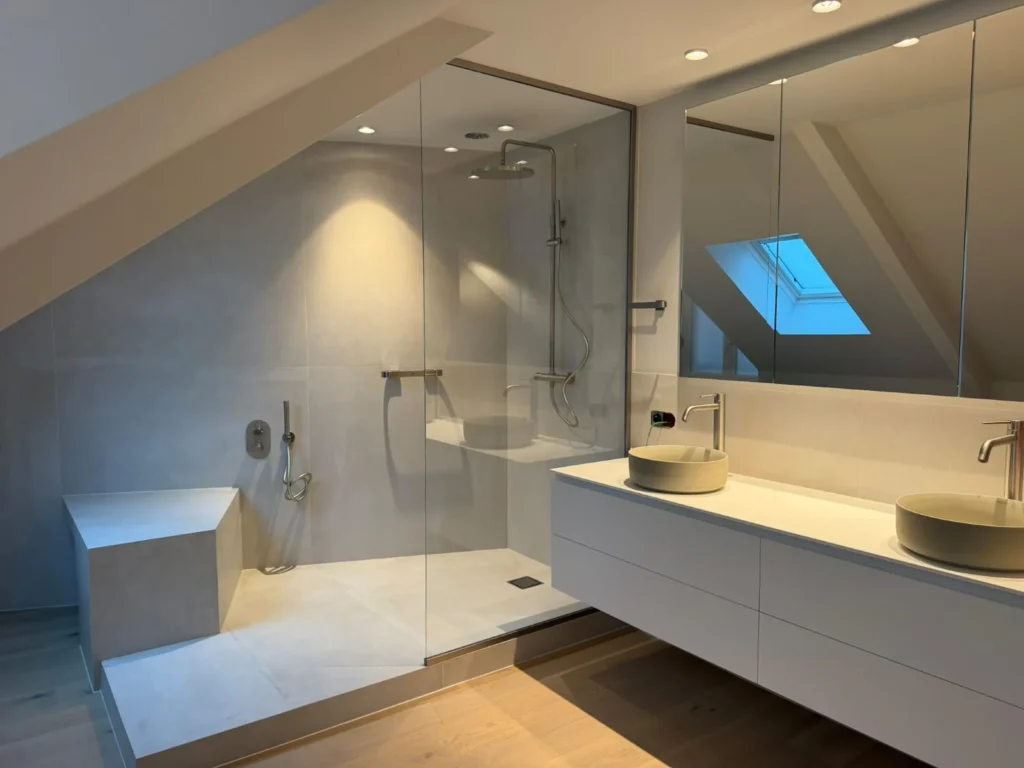 Salle de bains sous combles : douche vitrée, double vasque et fenêtre de toit