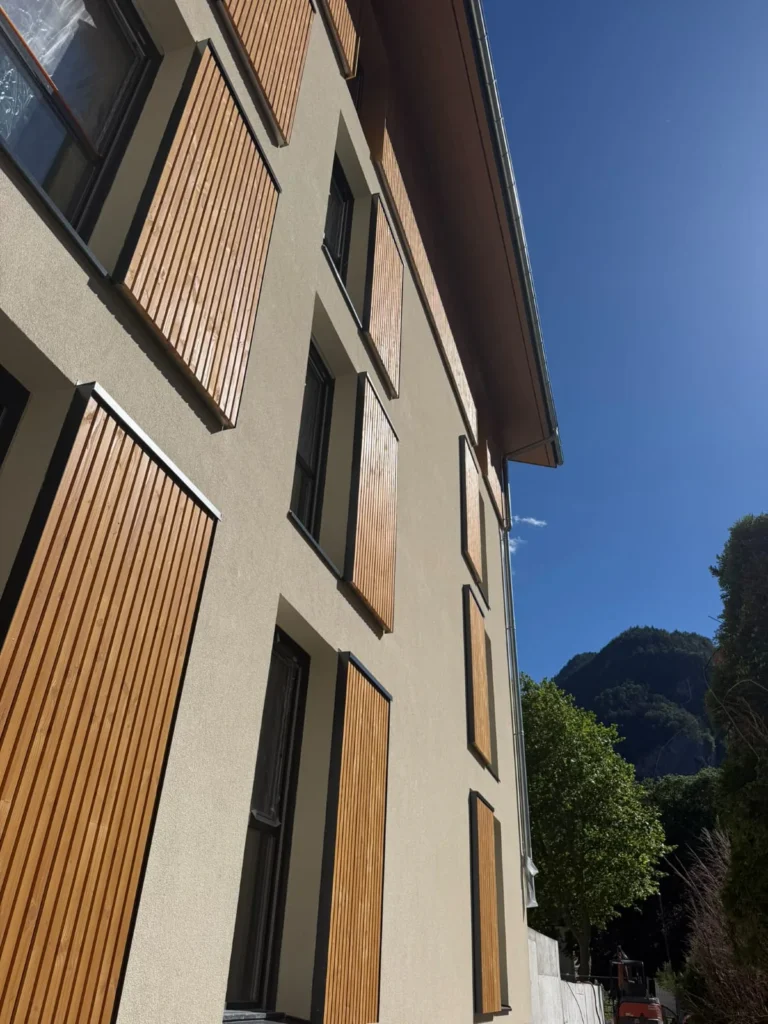 Façade enduite ton sable rythmée de panneaux à lames de bois verticales